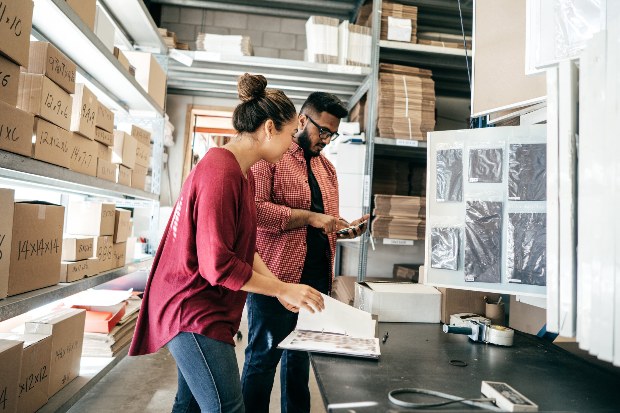 A man and a woman in a warehouse with packages looking at a computer