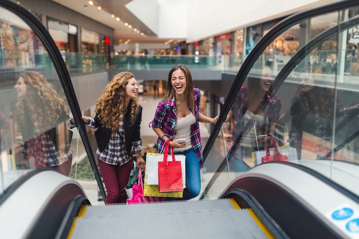 Two people holding shopping bags on escalator.