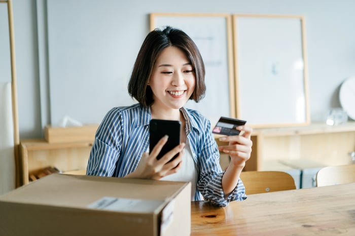 A smiling person entering credit card information into a smartphone making an e-commerce purchase.