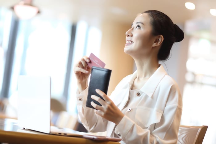 A woman pulling a credit card from her purse while sitting in front of a laptop.