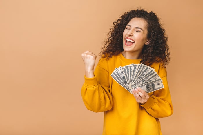 A woman gleefully holds $100 U.S. banknotes in her hand.