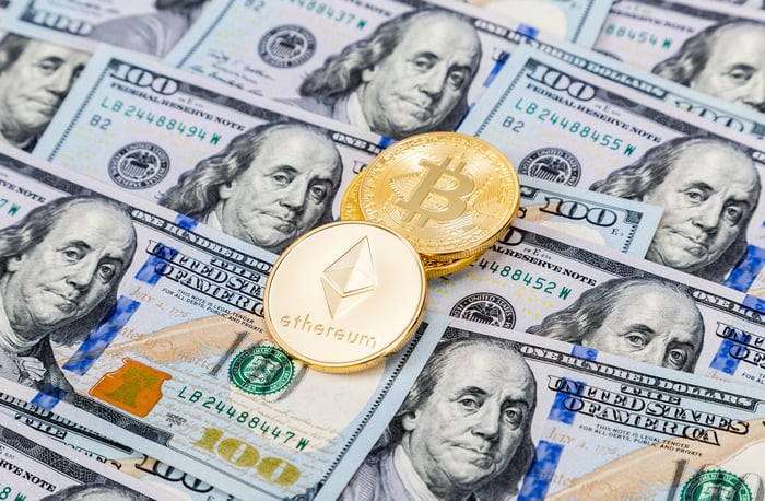 Golden Ethereum and Bitcoin coins resting on a pile of hundred-dollar bills.