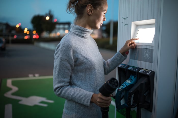 A person holding an electric vehicle charger while using the charging station's display board.