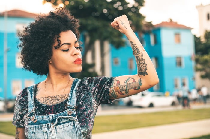 A person in overalls is flexing a bicep.