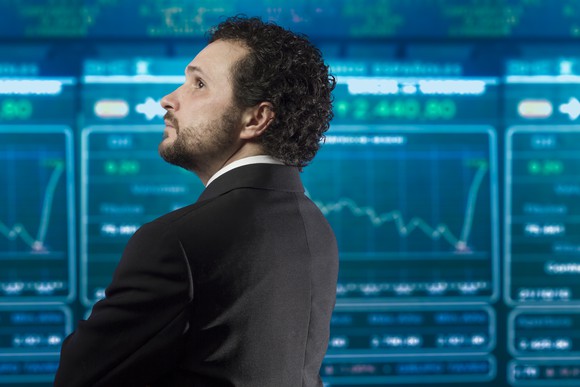 A businessperson looking at an electronic big board with stock charts and quotes.
