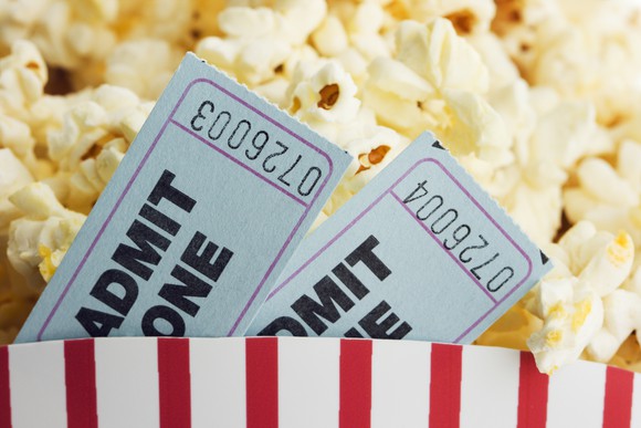 Two movie theater admission tickets stuffed into the side of a full tub of popcorn.