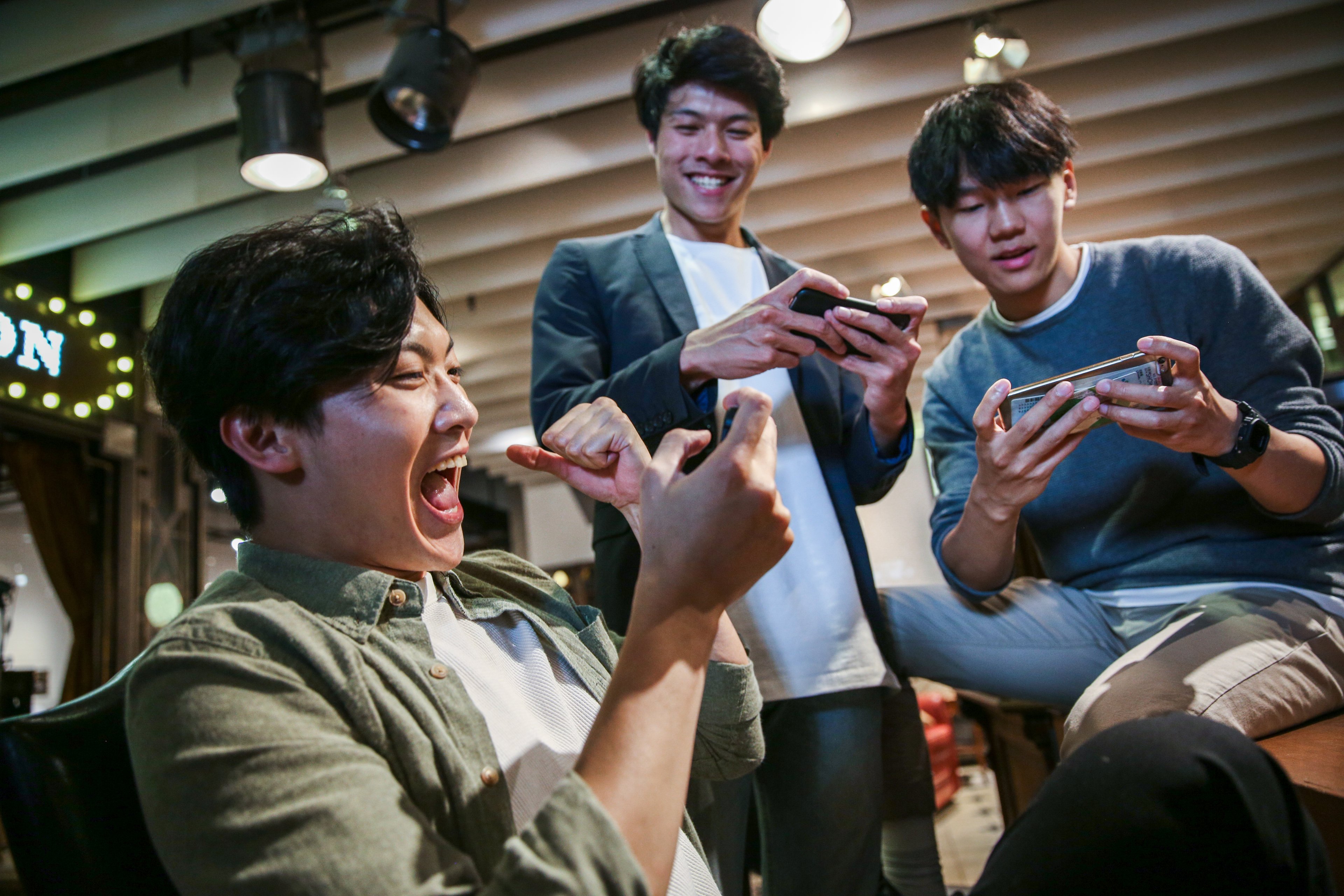 A group of three smiling friends playing games on their smartphones.