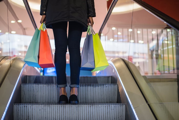 A shopper holding bags on an escalator in a mall.