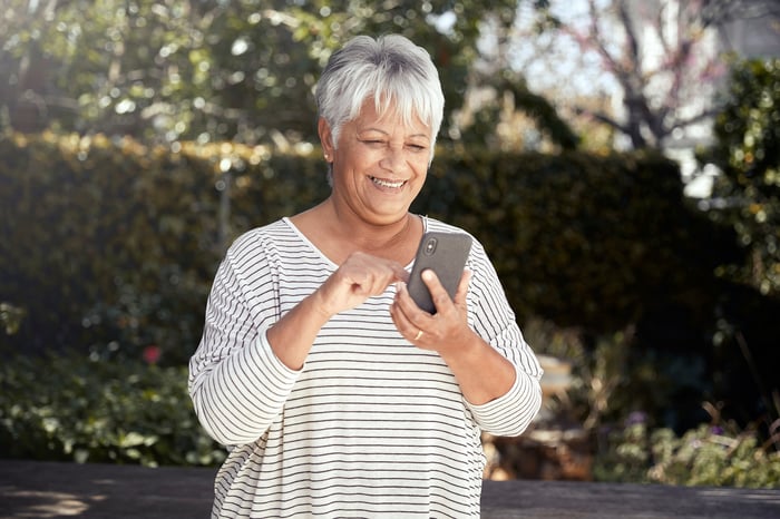 Smiling person outdoors using phone.