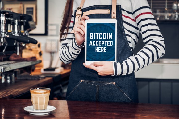 Coffee shop employee holding a bitcoin accepted here sign.