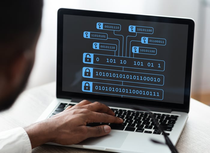 A person typing on a laptop, with the display screen showing encrypted blockchain with binary code. 