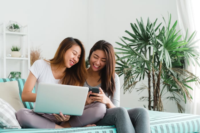 Two friends on couch with laptop and smartphone