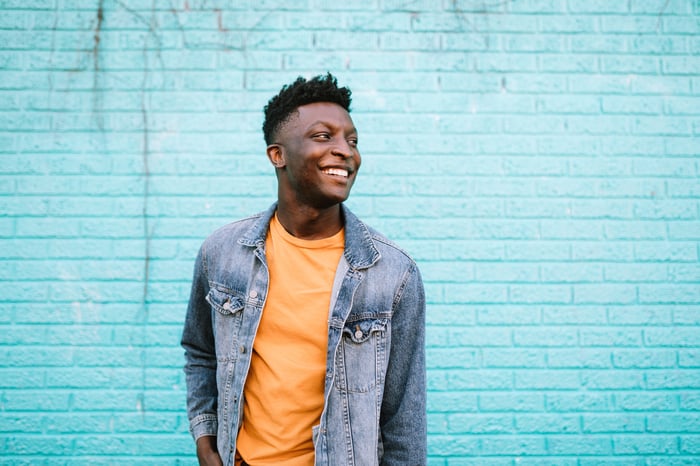 A person in casual clothing smiles while standing in front of a blue wall.
