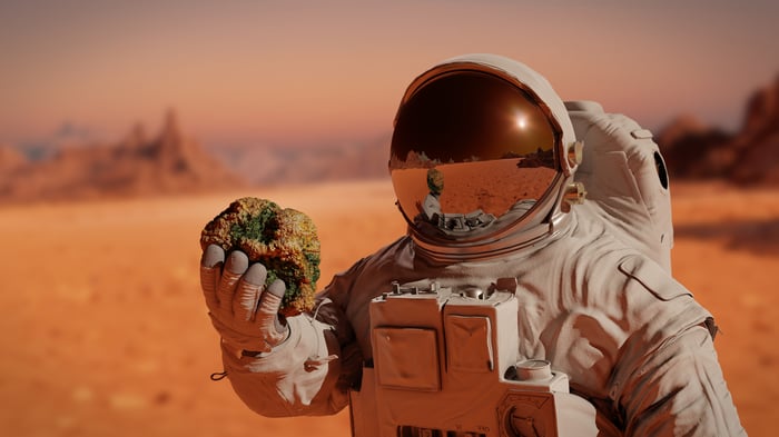 An astronaut holding a rock while standing on Mars.