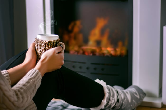 Person sitting in front of the fireplace holding cup of tea.