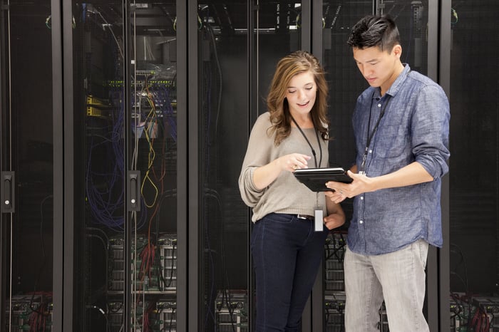 People viewing a tablet in front of stacks of supercomputers.