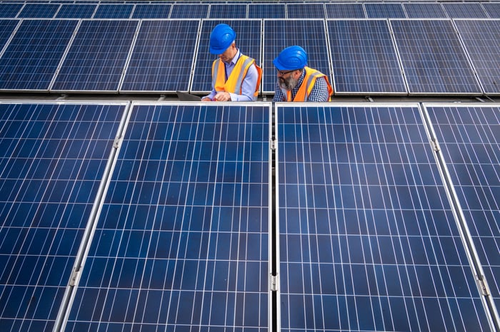 Technicians examine solar panels at a power facility.