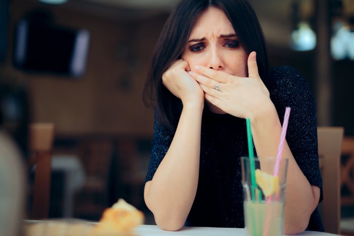 Woman seated at table, covering her mouth as if she's eaten something foul.