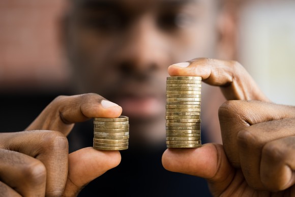 A person holding two stacks of coins, one double the size of another.