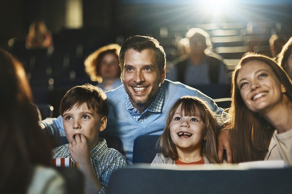 A happy family at the movies with other cinema-goers visible in the seats behind them.