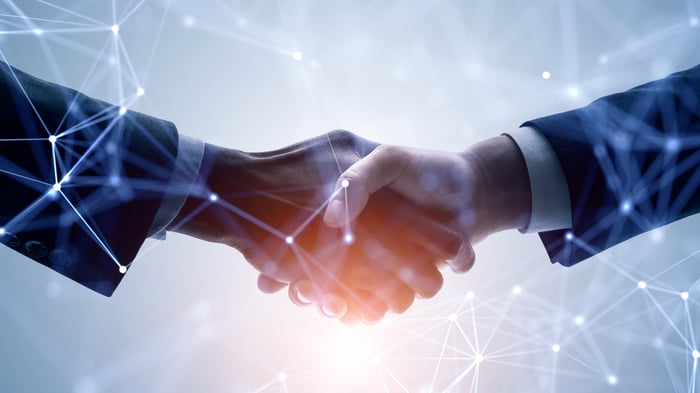 Two businesspeople shaking hands while surrounded by latticework representing blockchain smart contracts.
