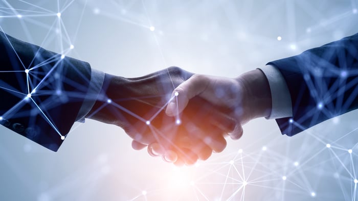 Two businesspeople shaking hands while surrounded by latticework representing blockchain smart contracts. 