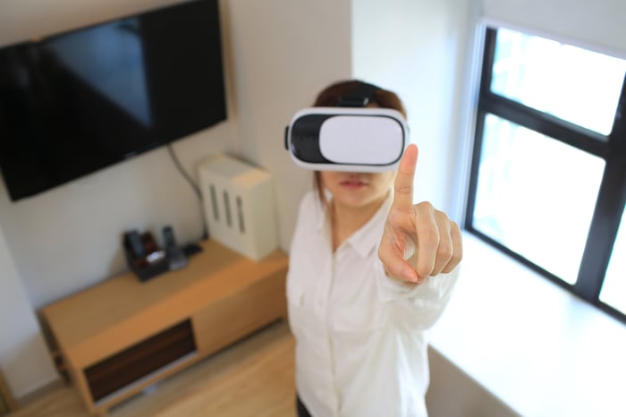 A top-down view of a person wearing a virtual reality headset and pointing at something in the virtual world. 