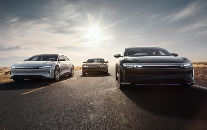Three Lucid Air electric vehicles on an asphalt road with the sun behind them.