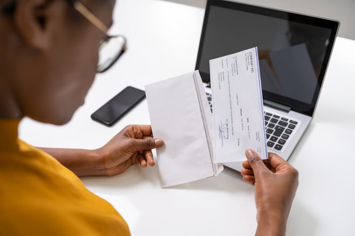 A person looking at a paycheck in front of a computer.