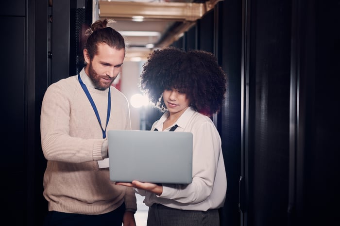 Two young professional looking at a laptop in a data center.