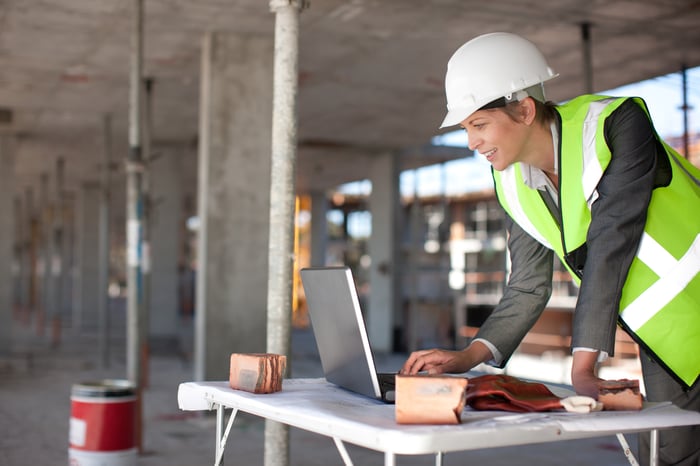 Someone in a hard hat uses a laptop on a remote job site.