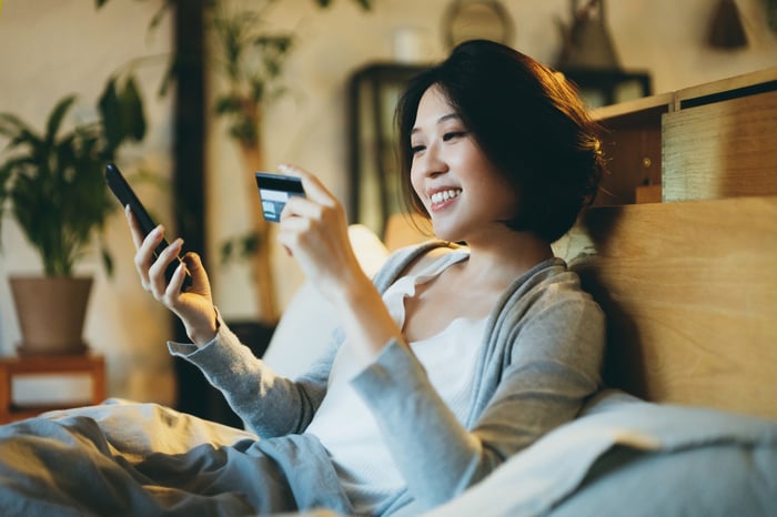 A person smiles while holding a smartphone in one hand and a credit card in the other.