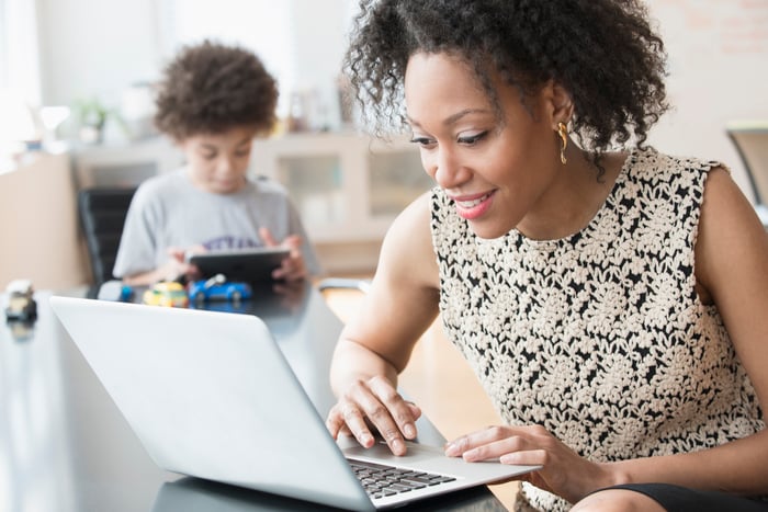 An investor, with a child in the background, looks at something on a laptop.