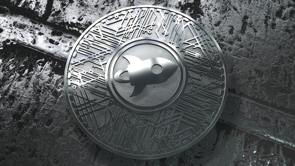 A silver-colored Stellar Lumen coin with a rocket ship logo.