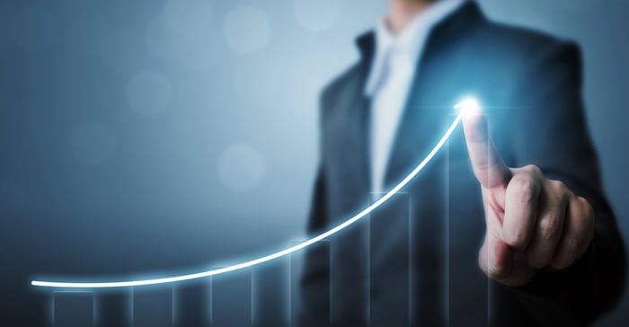 A person is pointing to a rising digital chart. 
