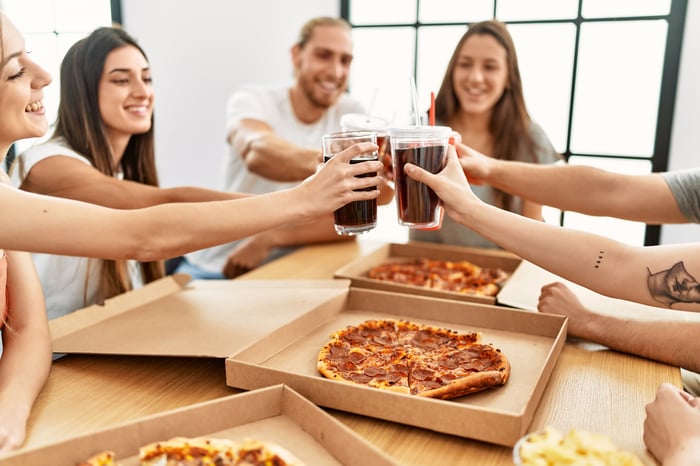 A group of people toast their glasses filled with cola.