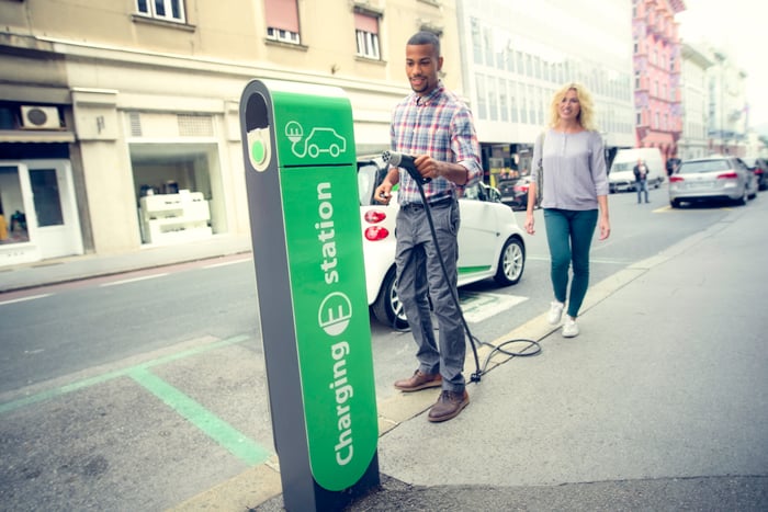 A person holding an electric car charging nozzle on the road to charge a car.