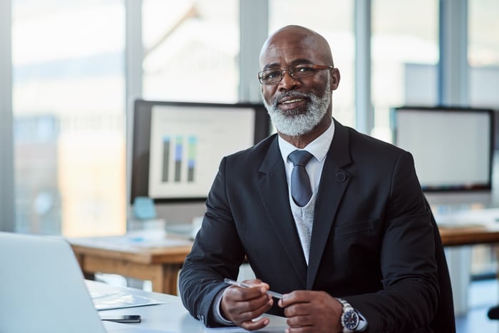 Smiling person in business suit seated at desk.