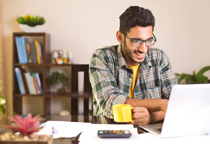 Smiling person holding mug at laptop.