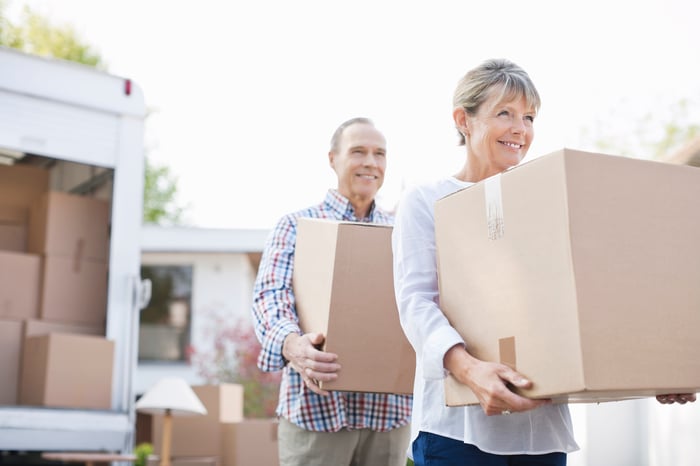 Two smiling people holding moving boxes.