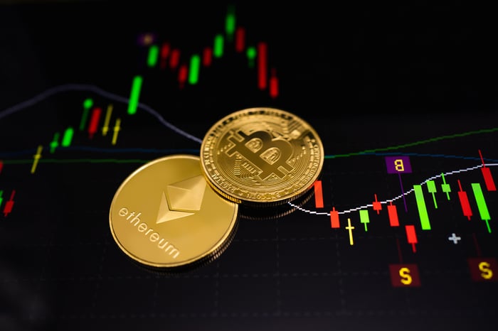 Two golden coins with Bitcoin and Ethereum logos on top of a pricing chart.