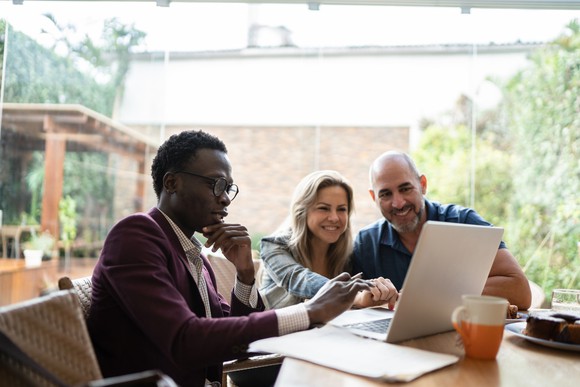 Three people sitting at a table with a laptop.