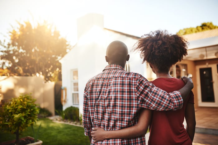 Two people with arms around each other looking at a house.
