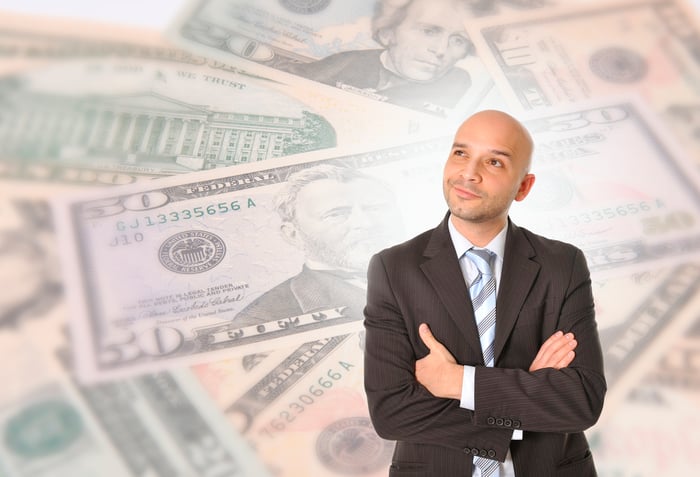 A person is seemingly thinking, with arms crossed, against a background of cash images.