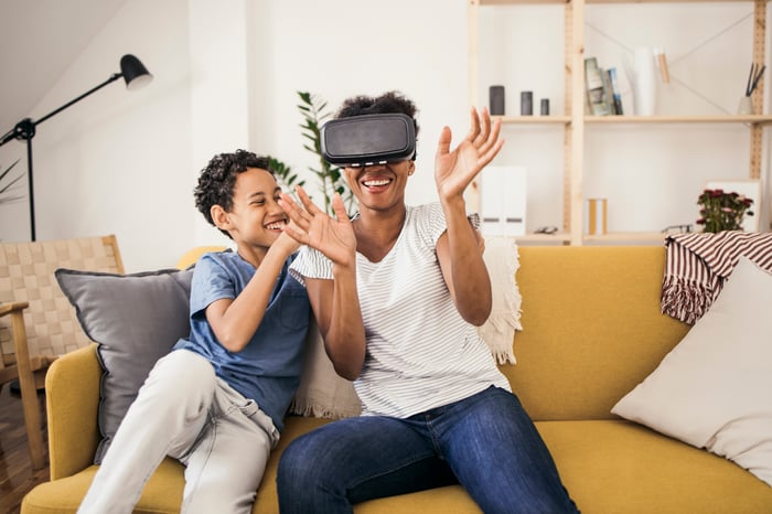 A parent wearing a virtual reality headset having fun on the couch with a child.