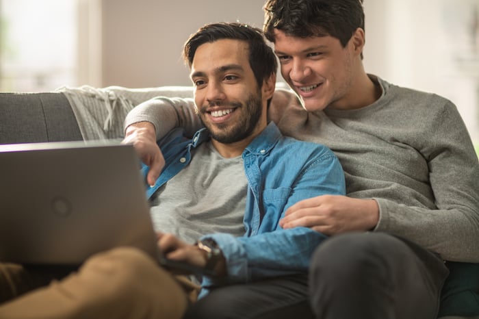 A couple on a couch is looking at a laptop and smiling.