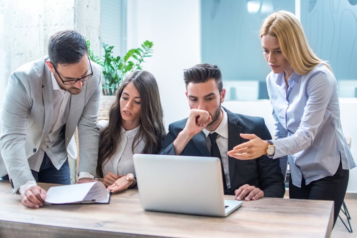 A group of people looking at a laptop and paperwork in an office.