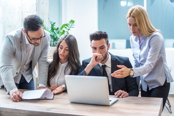 A group of people looking at a laptop and paperwork in an office.