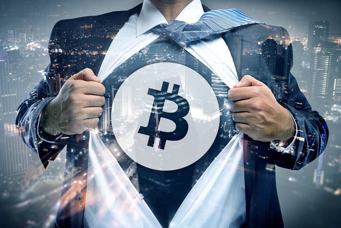Someone in a suit ripping open the buttoned shirt to reveal a t-shirt with the Bitcoin logo underneath.