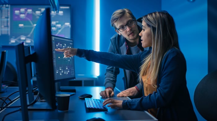 Two people looking concerned while analyzing data on computer screens.